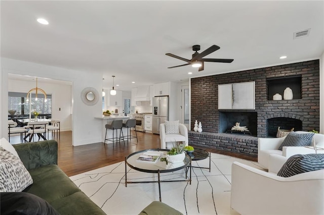 living area featuring a brick fireplace, visible vents, wood finished floors, and recessed lighting