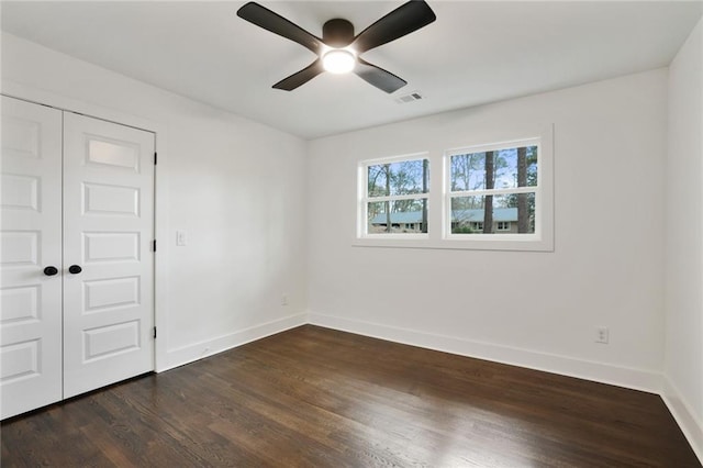 empty room featuring visible vents, dark wood-style flooring, a ceiling fan, and baseboards