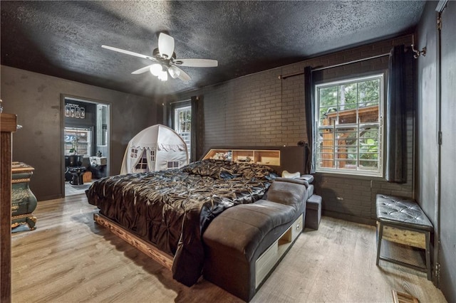 bedroom with ceiling fan, light hardwood / wood-style floors, brick wall, and multiple windows