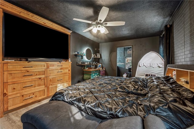 bedroom featuring a textured ceiling, light hardwood / wood-style flooring, ceiling fan, and brick wall