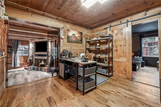 interior space with wooden ceiling, a barn door, wood walls, light hardwood / wood-style floors, and a tiled fireplace