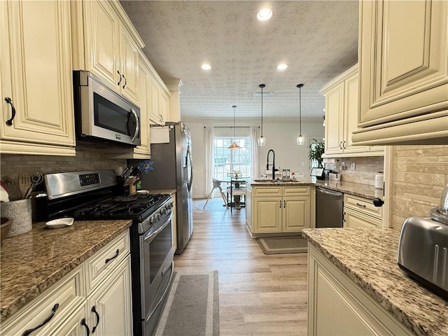 kitchen with stainless steel appliances, a peninsula, a sink, cream cabinetry, and light wood-type flooring