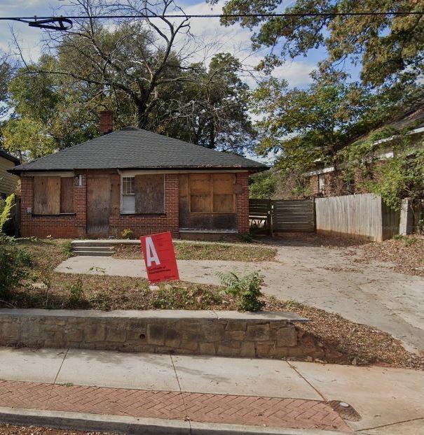 bungalow-style house with a shingled roof, a chimney, fence, and brick siding