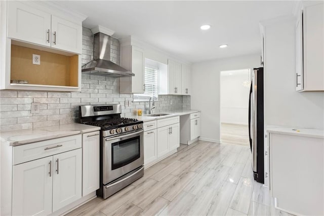 kitchen featuring appliances with stainless steel finishes, white cabinets, a sink, and wall chimney exhaust hood