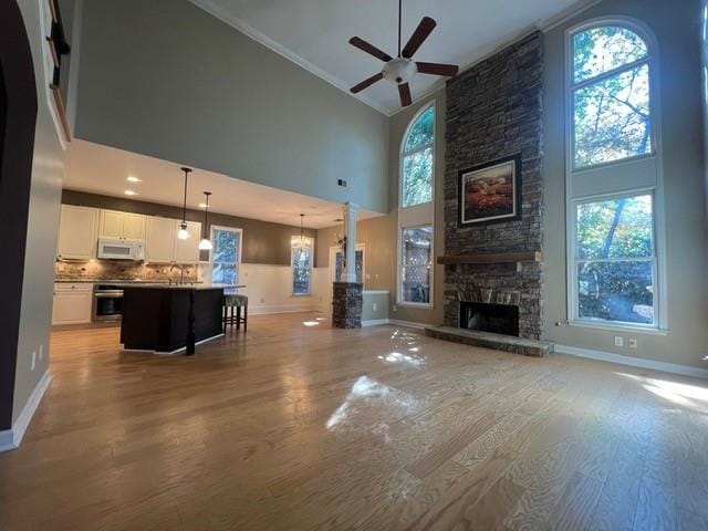 living room featuring ornamental molding, a towering ceiling, a stone fireplace, light wood-type flooring, and ceiling fan