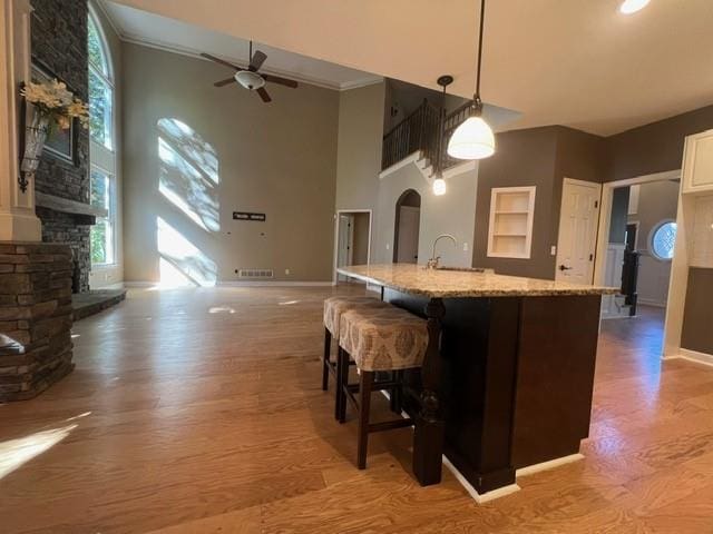 kitchen with a high ceiling, a stone fireplace, decorative light fixtures, and light hardwood / wood-style floors