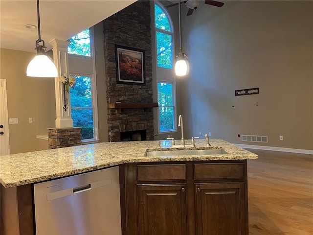 kitchen with sink, stainless steel dishwasher, a stone fireplace, light hardwood / wood-style flooring, and decorative columns