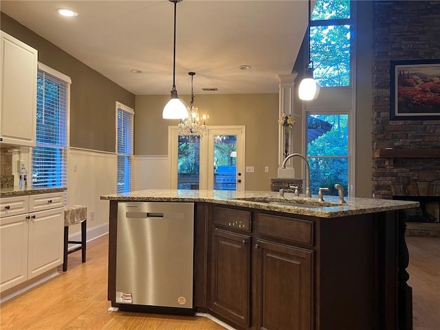 kitchen with dishwasher, hanging light fixtures, sink, a kitchen island with sink, and light wood-type flooring