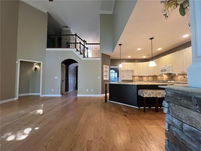 kitchen featuring white cabinetry, hanging light fixtures, a towering ceiling, light hardwood / wood-style flooring, and decorative backsplash