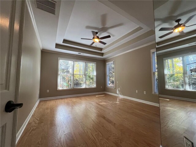 empty room with hardwood / wood-style floors, crown molding, and a raised ceiling