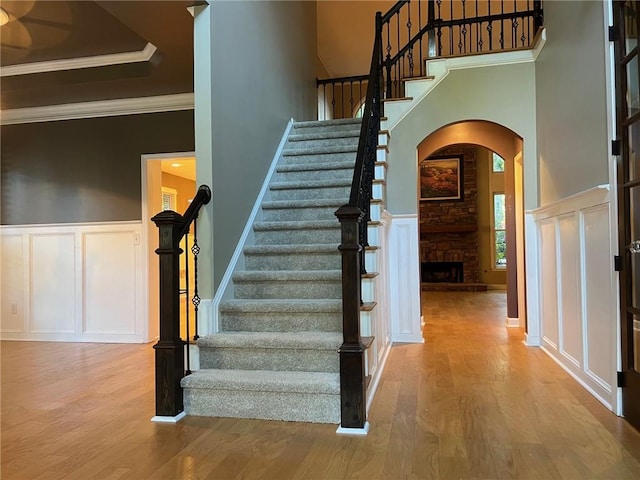 stairway with hardwood / wood-style floors, a high ceiling, a fireplace, and ornamental molding