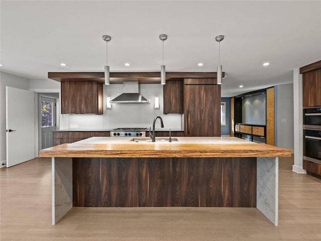 kitchen with a sink, hanging light fixtures, light wood-type flooring, wall chimney exhaust hood, and modern cabinets