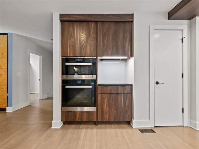 kitchen with double oven, visible vents, baseboards, light wood-style floors, and dark brown cabinets