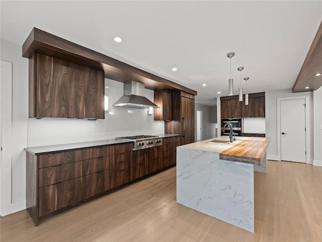 kitchen with stainless steel gas cooktop, a sink, wall chimney range hood, light wood-type flooring, and modern cabinets