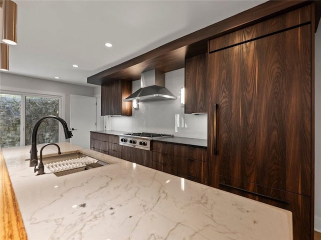 kitchen with a sink, wall chimney range hood, light stone countertops, modern cabinets, and stainless steel gas stovetop