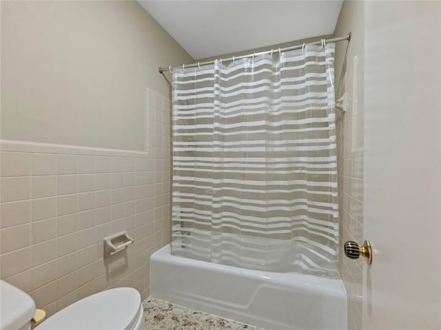 bathroom with toilet, shower / tub combo, tile walls, and a wainscoted wall