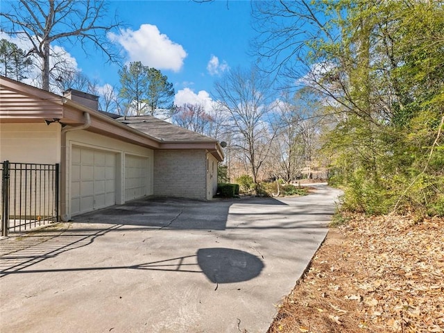 view of home's exterior featuring a garage, brick siding, driveway, and fence