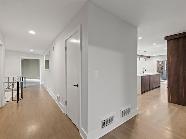 corridor with recessed lighting, visible vents, a sink, and light wood finished floors