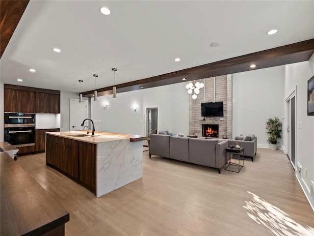 kitchen with light wood finished floors, a large fireplace, a sink, dark brown cabinetry, and modern cabinets