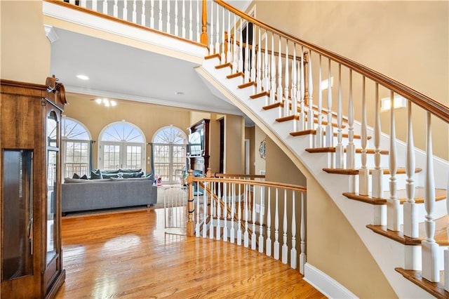 stairway featuring crown molding, a towering ceiling, and wood-type flooring