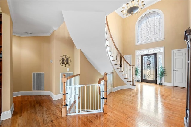 entrance foyer featuring a high ceiling, ornamental molding, a notable chandelier, and light wood-type flooring