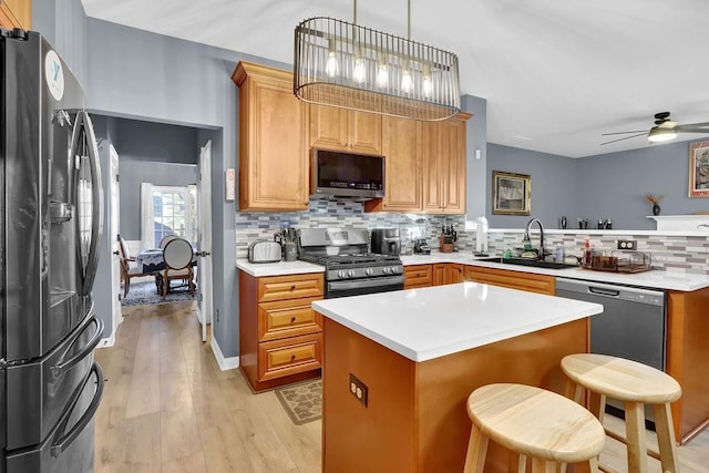 kitchen featuring ceiling fan, sink, stainless steel appliances, decorative light fixtures, and a breakfast bar