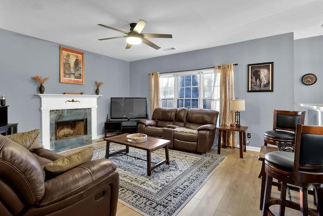 living room featuring ceiling fan, a high end fireplace, and light wood-type flooring