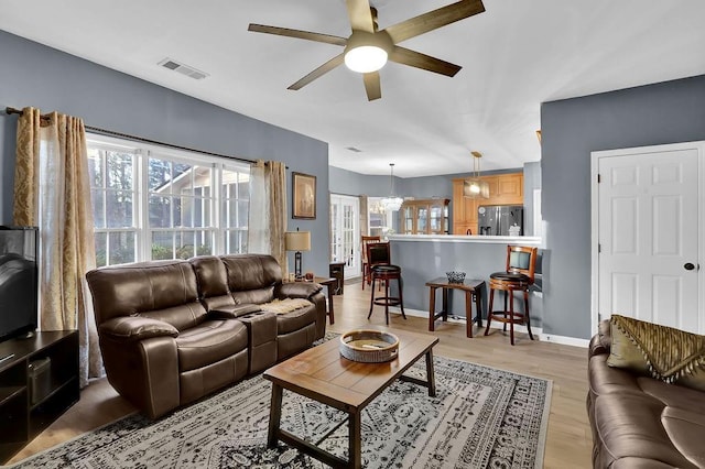 living room featuring ceiling fan with notable chandelier, light hardwood / wood-style flooring, and plenty of natural light