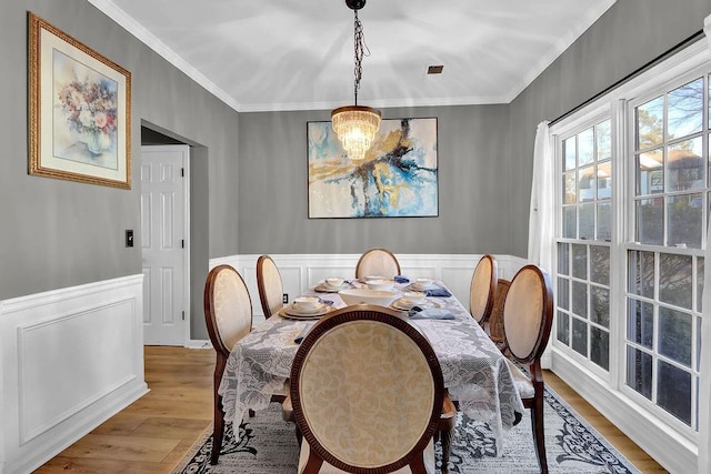 dining room with light wood-type flooring, ornamental molding, and an inviting chandelier