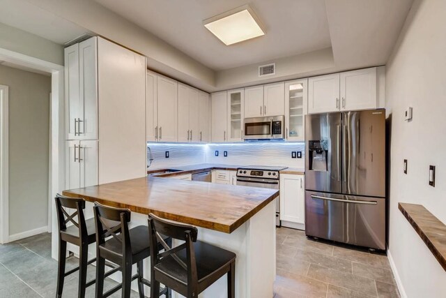 kitchen featuring visible vents, wooden counters, glass insert cabinets, decorative backsplash, and appliances with stainless steel finishes