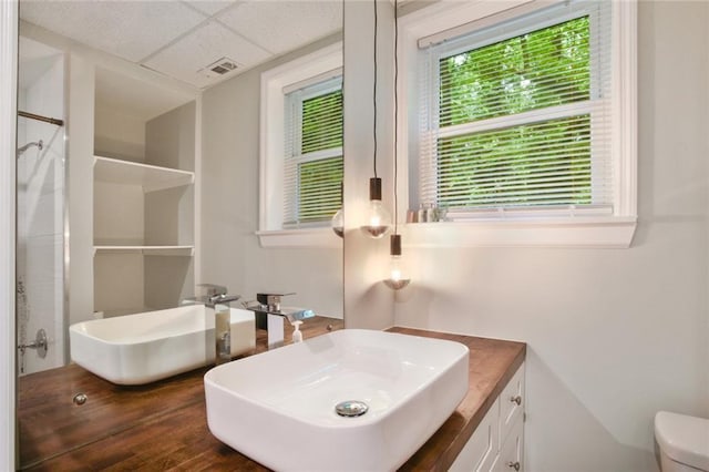 bathroom with visible vents, a paneled ceiling, toilet, vanity, and a shower