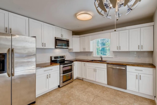 kitchen featuring light tile patterned floors, a sink, white cabinets, appliances with stainless steel finishes, and tasteful backsplash