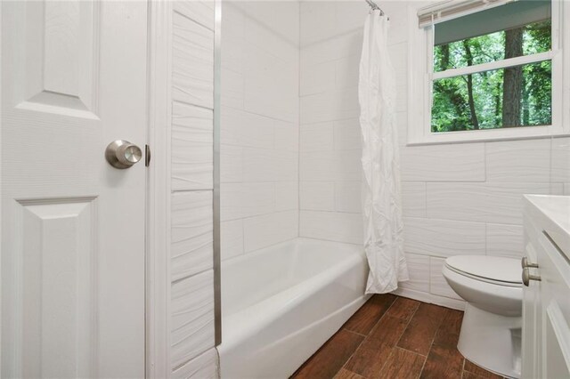 bathroom featuring tile walls, toilet, wood finished floors, vanity, and shower / bathtub combination with curtain