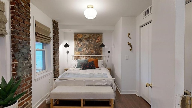 bedroom with dark hardwood / wood-style floors and brick wall