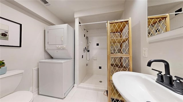 bathroom featuring sink, tile patterned flooring, stacked washer / drying machine, tiled shower, and toilet