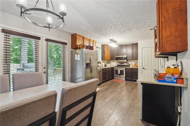 kitchen with an inviting chandelier, hardwood / wood-style flooring, a textured ceiling, appliances with stainless steel finishes, and decorative light fixtures