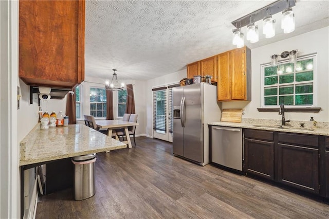 kitchen featuring kitchen peninsula, stainless steel appliances, dark wood-type flooring, sink, and decorative light fixtures