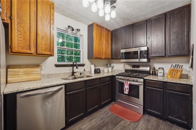 kitchen with sink, stainless steel appliances, light stone counters, dark hardwood / wood-style floors, and a textured ceiling