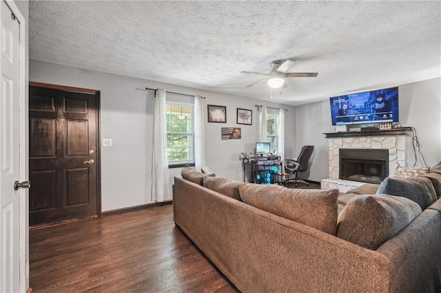 living room with dark hardwood / wood-style flooring, ceiling fan, a stone fireplace, and a textured ceiling