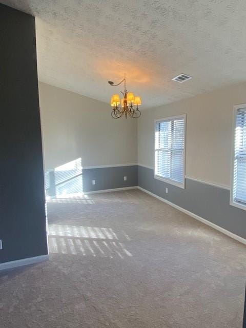 empty room with carpet, a textured ceiling, and an inviting chandelier