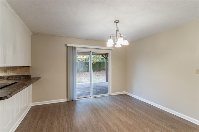 unfurnished dining area with a textured ceiling, ornamental molding, hardwood / wood-style flooring, and a chandelier