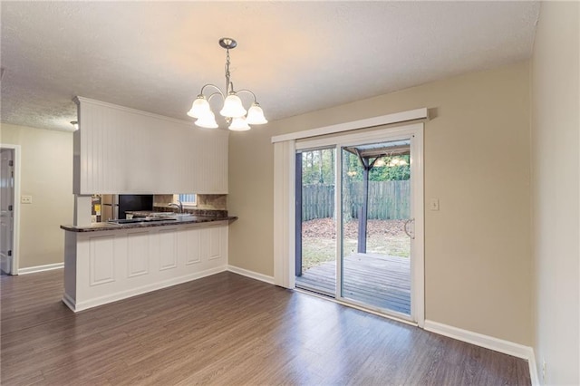 kitchen featuring dark wood-type flooring, pendant lighting, kitchen peninsula, and a notable chandelier