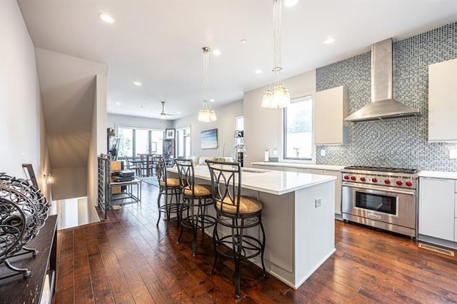 kitchen with a kitchen bar, dark wood-type flooring, premium range, wall chimney exhaust hood, and light countertops