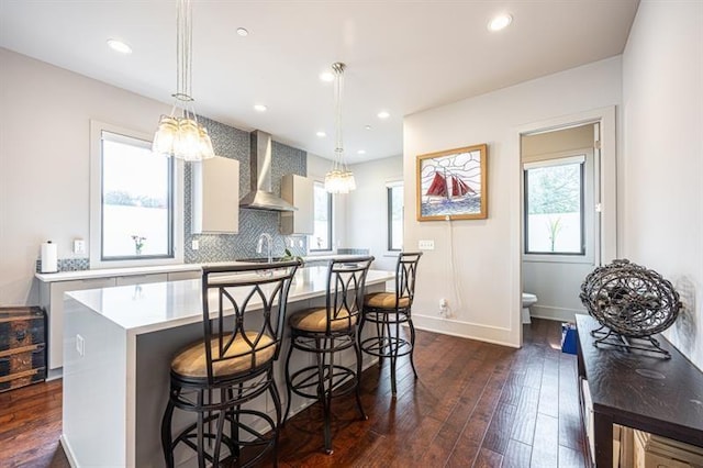 kitchen featuring a breakfast bar area, dark wood-style flooring, light countertops, and wall chimney range hood