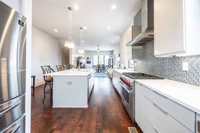 kitchen with visible vents, wall chimney range hood, an island with sink, decorative backsplash, and appliances with stainless steel finishes