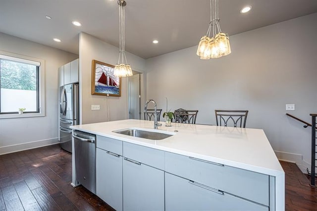 kitchen featuring a sink, stainless steel appliances, dark wood finished floors, and a center island with sink