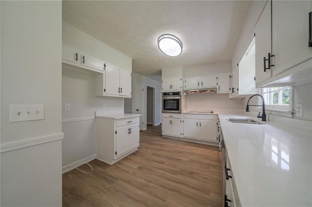4732 Manly Ct, Stone Mountain, GA 30088 - kitchen with stainless steel oven, white cabinetry, light wood-style floors, under cabinet range hood, and a textured ceiling
