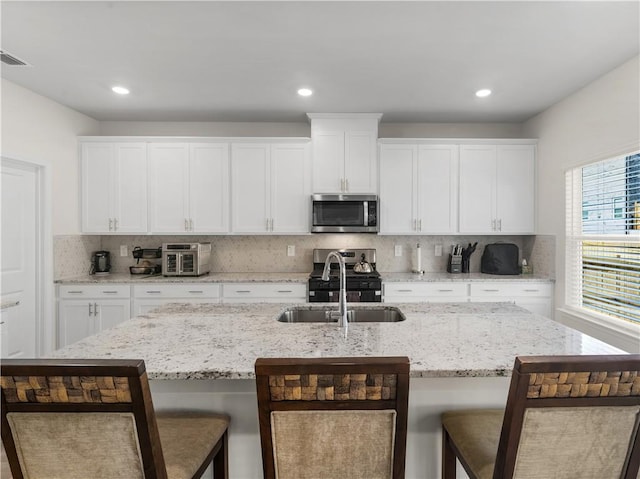 kitchen with a center island with sink, sink, a kitchen bar, white cabinetry, and stainless steel appliances