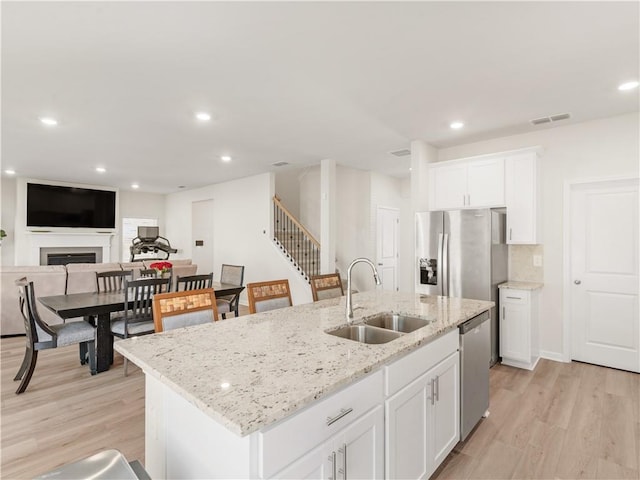 kitchen featuring white cabinets, sink, stainless steel appliances, and an island with sink