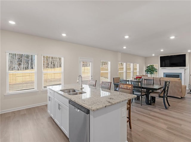 kitchen featuring a kitchen island with sink, sink, dishwasher, white cabinetry, and a breakfast bar area